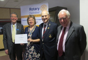 Three men and a woman holding a certificate standing in front of a Rotary banner