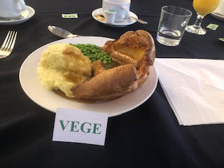 Generously sized toad-in-the-hole with mash and peas, with a card in front of the plate reading VEGE