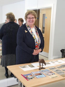A smiling lady standing behind a table bearing a wooden carving and publications