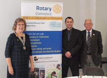 A woman wearing a chain of office standing with two men by a Rotary banner