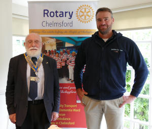 A short man with a white beard and wearing a chain of office standing on the left of a Club banner with a taller man, also bearded, standing on the right