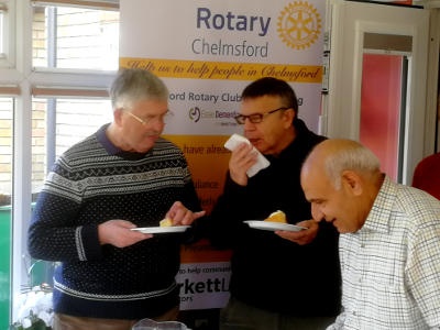 Three men, two of them eating, standing in front of a Rotary banner