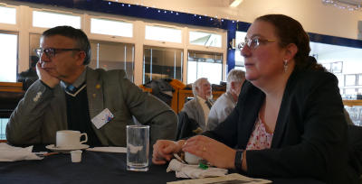 A man and woman sitting at a table with cups in front of them, looking puzzled