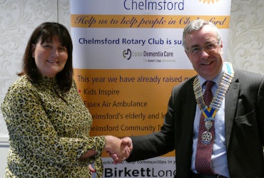 A long-haired woman and a grey-haired man standing in front of a Rotary banner