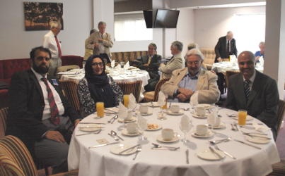 Four people sitting at a dining table with others in the background