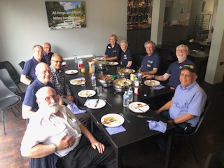 Smiling people wearing Rotary Club clothing and sitting either side of a long table