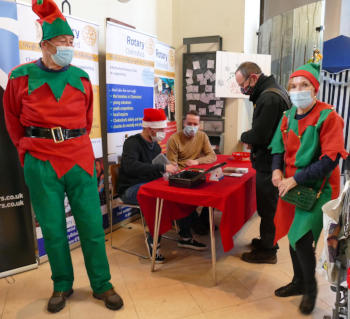 A man and a woman dressed as elves standing by a table with two people behind it