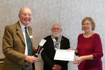 A man on the left with glasses holding a trophy, with a bearded man with a chain of office next to him and a woman holding a certificate to the right