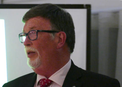 A dark-haired and bearded man wearing glasses and a suit