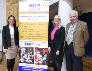 Two women and a man standing beside a Rotary banner