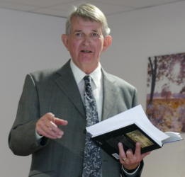 Grey-suited man speaking while holding a book