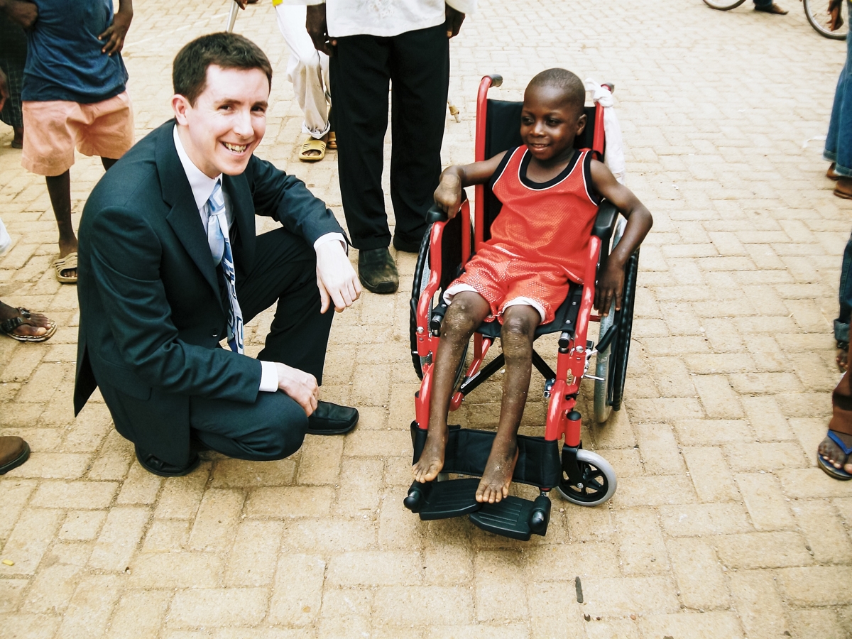 International Service - A child in his new wheelchair with Simon Harrington, who first travelled to Ghana in his work and recognised the problem there.