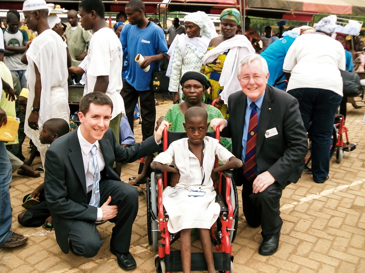 International Service - The recipient of one of the first batch of wheelchairs in Tamale village with Rtn. Stephen Harrington and his son Simon Harrington.
